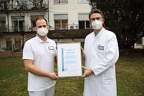 Zwei Ärzte halten gemeinsam ein Zertifikat hoch