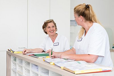 Zwei Pflegefachkräfte tauschen sich am Stationsstützpunkt aus